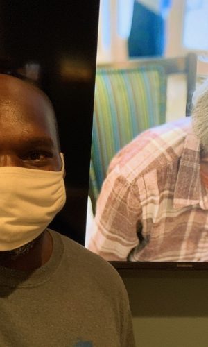 Anthony Wearing A Face Mask. Behind Him, A Picture of An Older Lady, A Happy Client. She's Smiling and Looking Down. Moving Services Around Seattle Area.